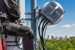Professional industrial climber in uniform and climber equipment on the telecommunication tower is installing outdoor unit to antenna for next adjustment. Working process of upgrading telecommunication equipment.