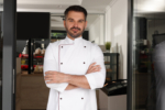 Happy baker/chef in uniform at door of his cafe
