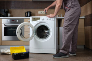 Appliance repairman disassembling a washing machine with a screwdriver. Professional repair of household appliances.