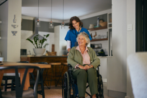 Mid adult happy nurse helping old woman in wheelchair with copy space at home. Smiling healthcare worker assisting an elderly woman in daily routine. Compassionate caregiver providing care for an aged disabled woman at home.