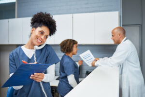 Team of healthcare professionals working together in a medical setting. A smiling nurse coordinates tasks while communicating via phone, and colleagues consult documents, emphasizing teamwork in a professional healthcare environment.