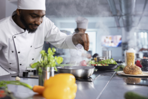 African american male chef sprinkles fresh basil over a plated dish